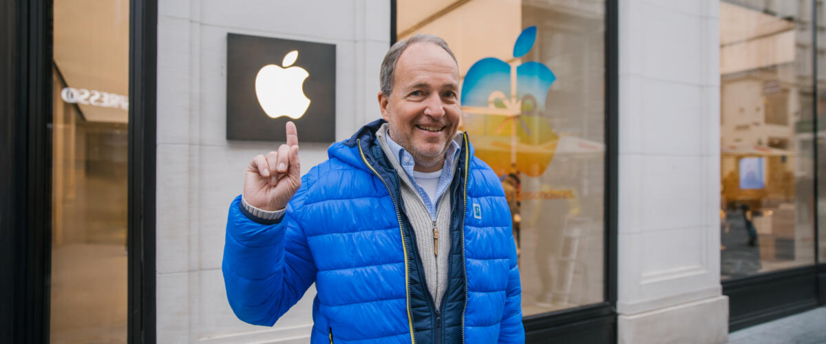 Bernhard Kloucek zeigt vor einem Geschäft mit dem zZeigefinger auf ein leuchtendes Apple-Logo