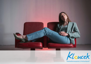 junge Frau auf einem roten Sofa liegen und wartend in die Kamera schauend